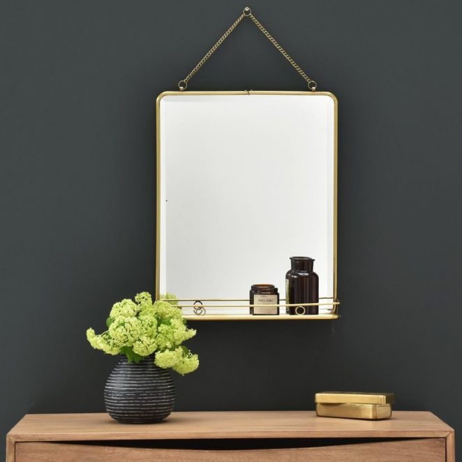 This rectangular brass mirror has a shelf that provides storage space in the hallway.